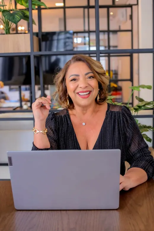Cristina Marinho sorrindo em frente ao notebook, no escritório da clínica