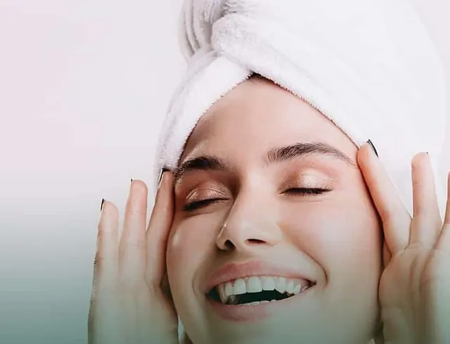 Mulher sorrindo com a pele luminosa e uma toalha branca no cabelo